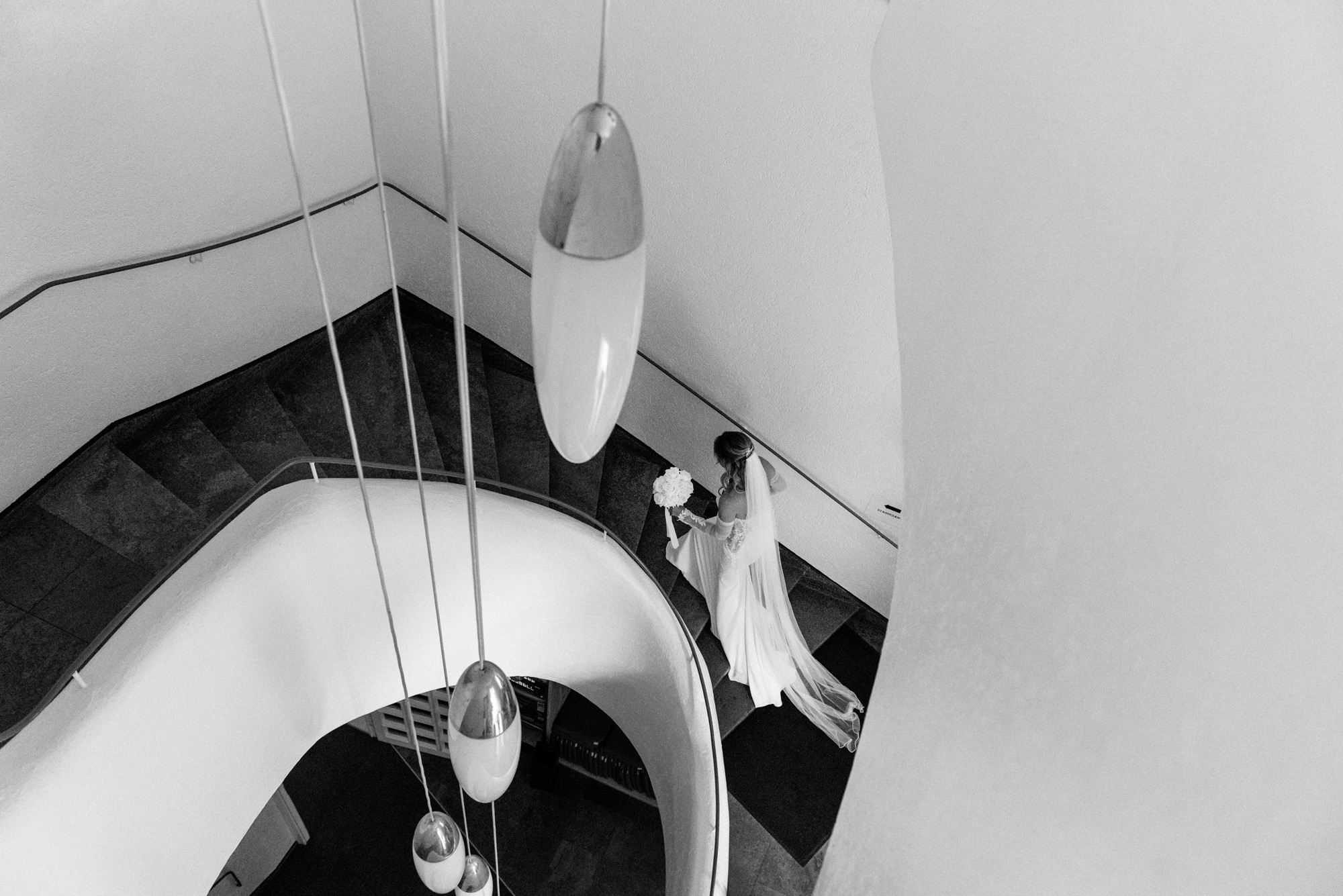 braut-treppe-schwarz-weiss-hochzeitsfotografie.jpg Braut mit Brautstrauß und langem Schleier auf einer geschwungenen Treppe